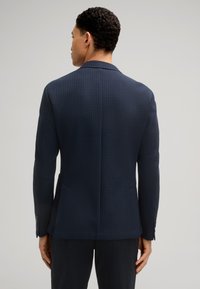 Marineblauwe gestreepte blazer met gestructureerde schouders, twee zijzakken en knoopaccenten op de mouwen. Glad stof met een getailleerde pasvorm.