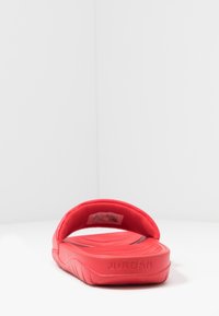 Punane libisemisjalats laia rihmaga ja tekstuurse materjaliga. Tekst "JORDAN" on tallal embosseeritud. Kerge ja mõeldud igapäevaseks kandmiseks.