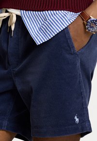 Marina kordjumshorts med ribbat mönster, med en sidoficka och en liten broderad logotyp. I kombination med en blårandig skjorta och en klocka.