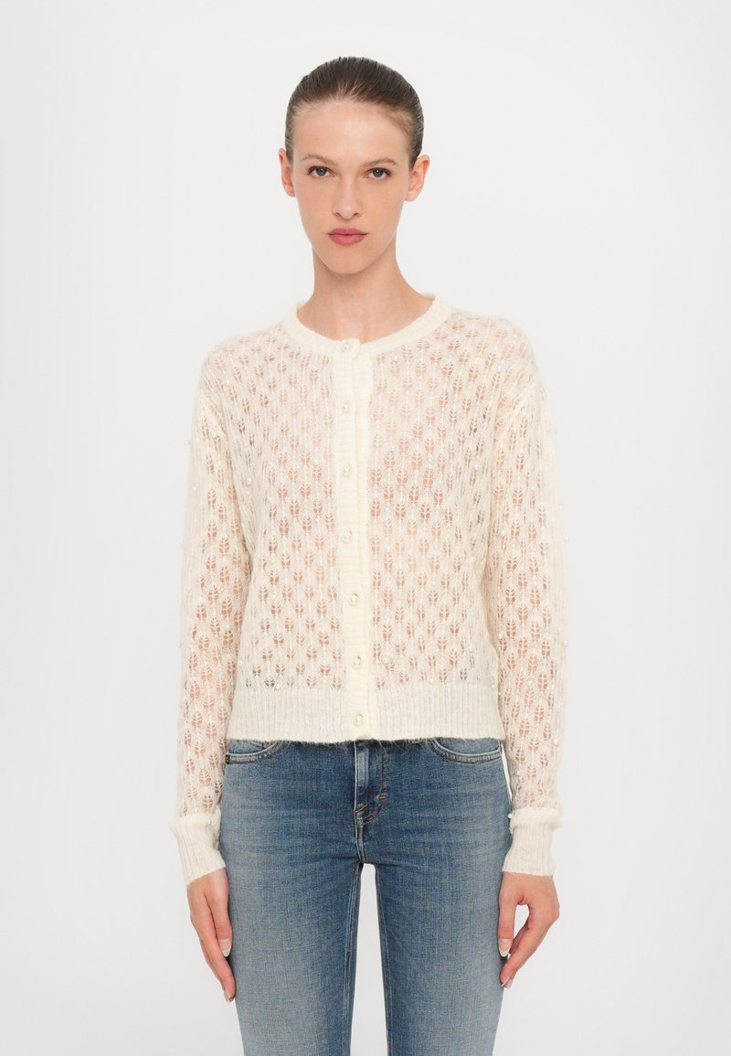 Cardigan lavorato a maglia in crema con motivo traforato, scollo rotondo e bottoni perlacei. Presenta maniche lunghe e un orlo accorciato.