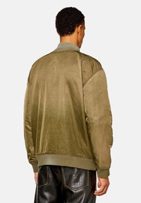 Olivgrön bomberjacka i smidigt material, med ribbad krage och manschetter, samt en texturerad yta på baksidan.