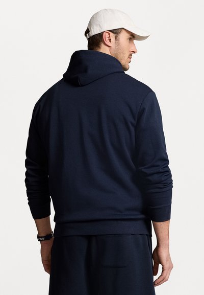 Tamsiai mėlynas džemperis su raišteliu, banguotais rankogaliais ir apačia. Minkšta, tekstūrinė medžiaga. Dėvimas su derančiomis tamsiomis kelnėmis.