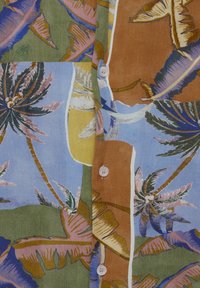 Boutons sur un tissu multicolore avec des motifs de feuilles de palmier en tons verts, bleus, marron et violet.