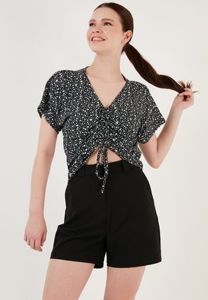 Black and white patterned short-sleeve cropped top with a tie front, paired with black shorts. Smooth texture and relaxed fit.