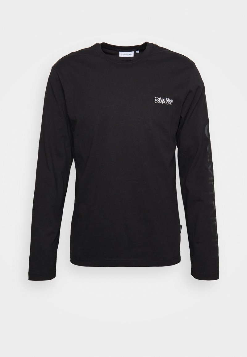 Svart långärmad t-shirt i bomull, med en liten vit logotyp på bröstet och text på vänster ärm. Slät yta.