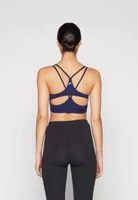 Navy sports bra with a cutout back design, featuring multiple crisscross straps. Stretchy fabric with a smooth texture, paired with black leggings.