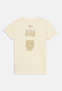 T-shirt en coton couleur crème avec une impression graphique d'une chaussure et un logo en doré au dos. Design à manches courtes et col rond.