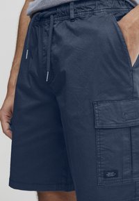 Pantaloni scurți cargo bleu marin cu talie elastică, șnur ajustabil, buzunare laterale și un buzunar mare în partea stângă a piciorului.