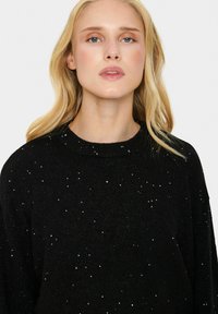 Schwarzer Pullover mit Rundhalsausschnitt, aus strukturiertem Stoff mit verstreuten silbernen Pailletten für zusätzlichen Detailreichtum.