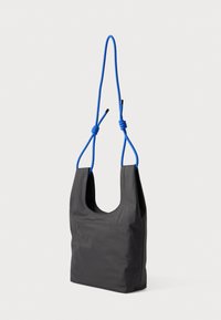 Μαύρη υφασμάτινη τσάντα με μαλακή υφή, διαθέτοντας μπλε νάιλον ιμάντες ώμου δεμένους πάνω και ένα κυρτό, ανοιχτό σχέδιο.