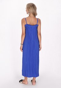 Königsblaue, plissierte Maxikleid mit dünnen Trägern und Rüschenausschnitt. Glatte Stofftextur, reicht bis zum Knöchel, kombiniert mit flachen Sandalen.