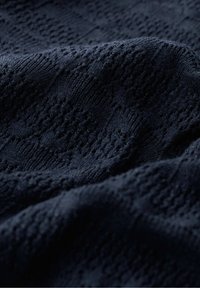 Námořnická modrá pletenina s texturovaným vzorem, která má otvorové vzory a jemnou, flexibilní strukturu.