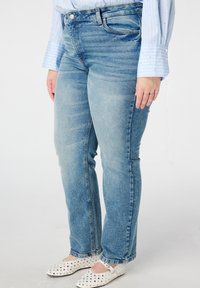 Lichtblauwe spijkerbroek met een klassieke vijfzakkenontwerp, licht vervaagd, rechte pijp, gedragen met plat schoenen met polka-dot textuur.