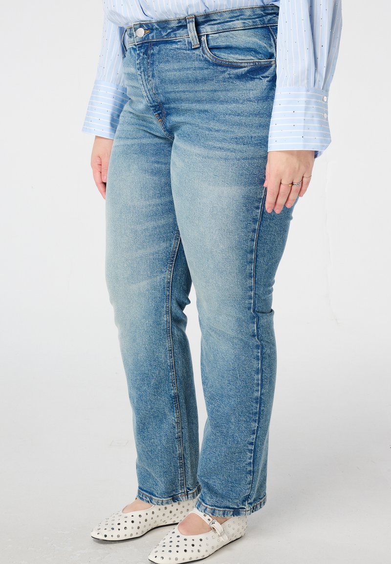 Lichtblauwe spijkerbroek met een klassieke vijfzakkenontwerp, licht vervaagd, rechte pijp, gedragen met plat schoenen met polka-dot textuur.