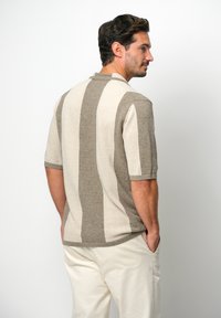 Polo a maniche corte, realizzato in maglia, con strisce alternate di beige chiaro e taupe. Tessuto testurizzato con colletto e vestibilità comoda.