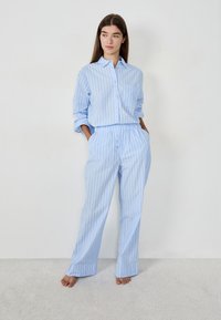 Camisa de botón de algodón a rayas en azul claro, combinada con pantalones de tiro ajustable a juego. Presenta un bolsillo en el pecho y un corte relajado.