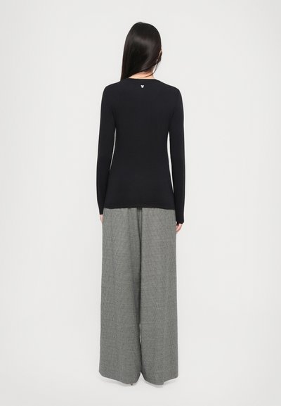 Long-sleeve black top with a fitted shape, paired with wide-leg gray patterned trousers, featuring a textured fabric and relaxed silhouette.