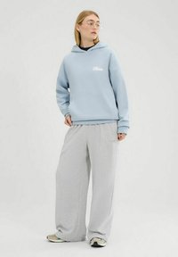 Sudadera azul claro con marca blanca, combinada con pantalones de chándal grises sueltos. El conjunto presenta un diseño casual con un ajuste cómodo.
