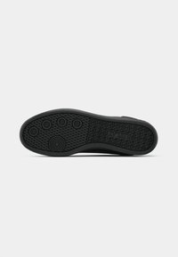 Black rubber shoe sole with circular and textured patterns, featuring rounded grips and a flat design for stability.