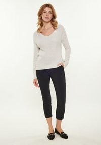 Ljust beige stickad tröja med V-hals, långa ärmar och ett texturerat mönster, i kombination med svarta cropped byxor och svarta slip-on skor.