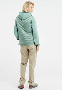 Šviesiai žalia izoliuota striukė su išsiuvinėjimu, smulkaus rašto rankovėmis ir pritvirtinta kapišonu. Bežinės kelnės ir daugiaspalviai žygio batai užbaigia įvaizdį.