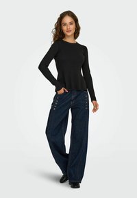 Haut noir à manches longues avec un col rond, associé à un pantalon en denim bleu à jambes larges doté de détails en œillets sur les côtés et de lacets.