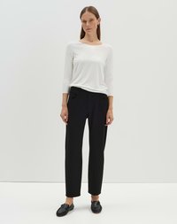 Chemise blanche à manches longues, pantalon noir ajusté et chaussures noires à enfiler. Texture lisse ; design simple avec une coupe classique et un décolleté ouvert.