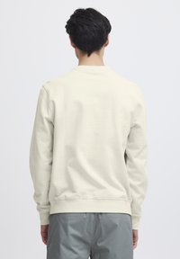 Hellbeige Sweatshirt mit langen Ärmeln, rundem Ausschnitt und glatter Textur. Verfügt über gerippte Bündchen und Saum, von hinten dargestellt.