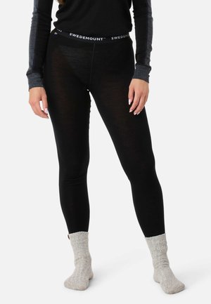 Beine in schwarzen Swedemount-Leggings, grauen Stricksocken und einem schwarzen Langarmshirt mit grauen Ärmeldetails, stehend auf weißem Hintergrund.