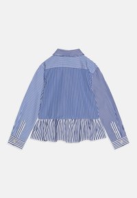 Randig blus i blått och vitt med långa ärmar, volangnederdel och knappmanschetter. Har en krage och en slät tygtextur.