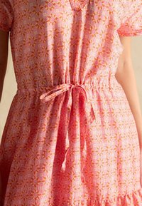 Ružové šaty s vzorom a elastickým pásom, so kvetinovým motívom v svetloružovej a oranžovej farbe. Mäkká tkanina a voľný strih.