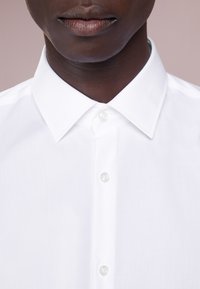 Bílá bavlněná košile s klasickým límcem a předním zapínáním na knoflíky, s hladkou texturou a jemným leskem.