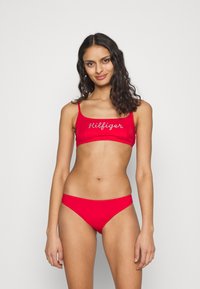 Set bikini rosso con top corto a spalline sottili e slip a vita bassa coordinati. Il top presenta la scritta "Hilfiger" ricamata in bianco.