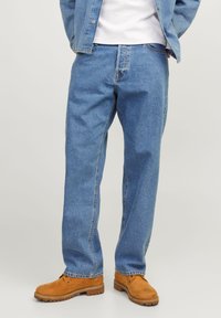 Jeans de ganga azul claro com um ajuste solto, apresentando um design clássico de cinco bolsos, costuras robustas e detalhes em metal de latão.