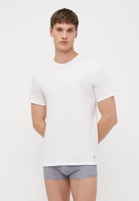T-shirt blanc à manches courtes en tissu lisse, avec un col rond et une coupe ajustée. Uni, sans motifs ni accents.