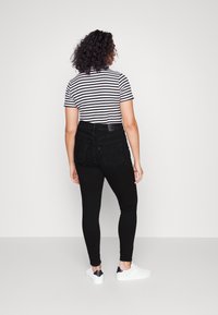 Vaqueros negros de cintura alta con bolsillos traseros, combinados con una camiseta ajustada de rayas blancas y negras. Zapatillas blancas completan el conjunto.