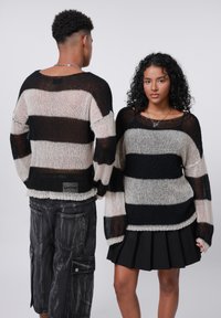 Maglione a righe in maglia nera e beige, con maniche lunghe e scollo ampio. Stile pullover con orlo leggermente sfilacciato.