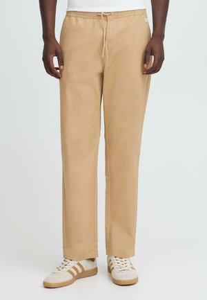 Pantalones caqui con cintura elástica y cordón, con corte recto, textura suave y bolsillos laterales. Combinados con zapatillas blancas.