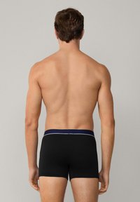 Boxer briefs neri con un design semplice, caratterizzati da una vita blu navy con una linea di accento bianca. Il materiale sembra liscio e aderente.