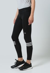 Svarta träningstights med en åtsittande design, med vita tre-stripes-accenter vid vaden och en elastisk midja. Tillverkade av stretchigt tyg.