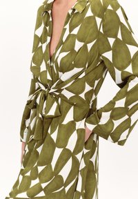 Vestito camicia verde e bianco con motivo, colletto, maniche lunghe, chiusura a bottoni e vita stretta con un grande fiocco. La trama del tessuto sembra morbida.