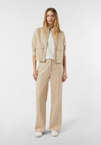 Beżowa kurtka bomberka z dwoma przednimi kieszeniami, zestawiona z beżowymi szerokimi spodniami. Dopełnieniem stroju jest wygodna biała koszulka i lekkie sneakersy.