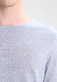 T-shirt à col rond à rayures bleues en tissu léger ; présente une texture douce avec des lignes horizontales subtiles et une encolure décontractée.