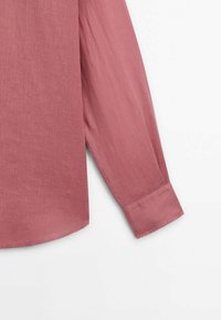 Chemise à manches longues couleur rose poudré avec un poignet à un seul bouton et un ourlet droit, présentée sur fond blanc.