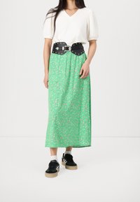 Grøn blomstrede maxi-nederdel med et sort læderbælte med sølvnitter, parret med sorte sneakers og en hvid puffærmet top.