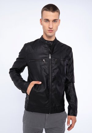 Chaqueta de cuero negra con cuello alto, cierre frontal de cremallera, dos bolsillos en el pecho con cremallera y una textura suave.