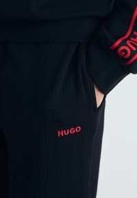 Schwarze Strick-Jogginghose mit strukturiertem Design, rotem gesticktem "HUGO"-Logo und eng anliegendem Bund mit Taschenverarbeitung.