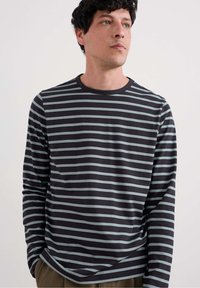 Pitkähihainen paita, jossa on laivaston sinisiä ja vaaleansinisia vaakasuoria raidoita, pyöreä pääntie, pehmeä kangas ja rento istuvuus. Ei suuria logoja tai grafiikoita.