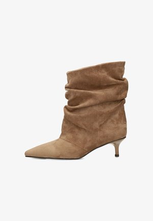 Brauner Wildleder-Stiefel mit lockerem Schaft, spitzer Zehenform und niedrigem beigen Katzenabsatz auf weißem Hintergrund.
