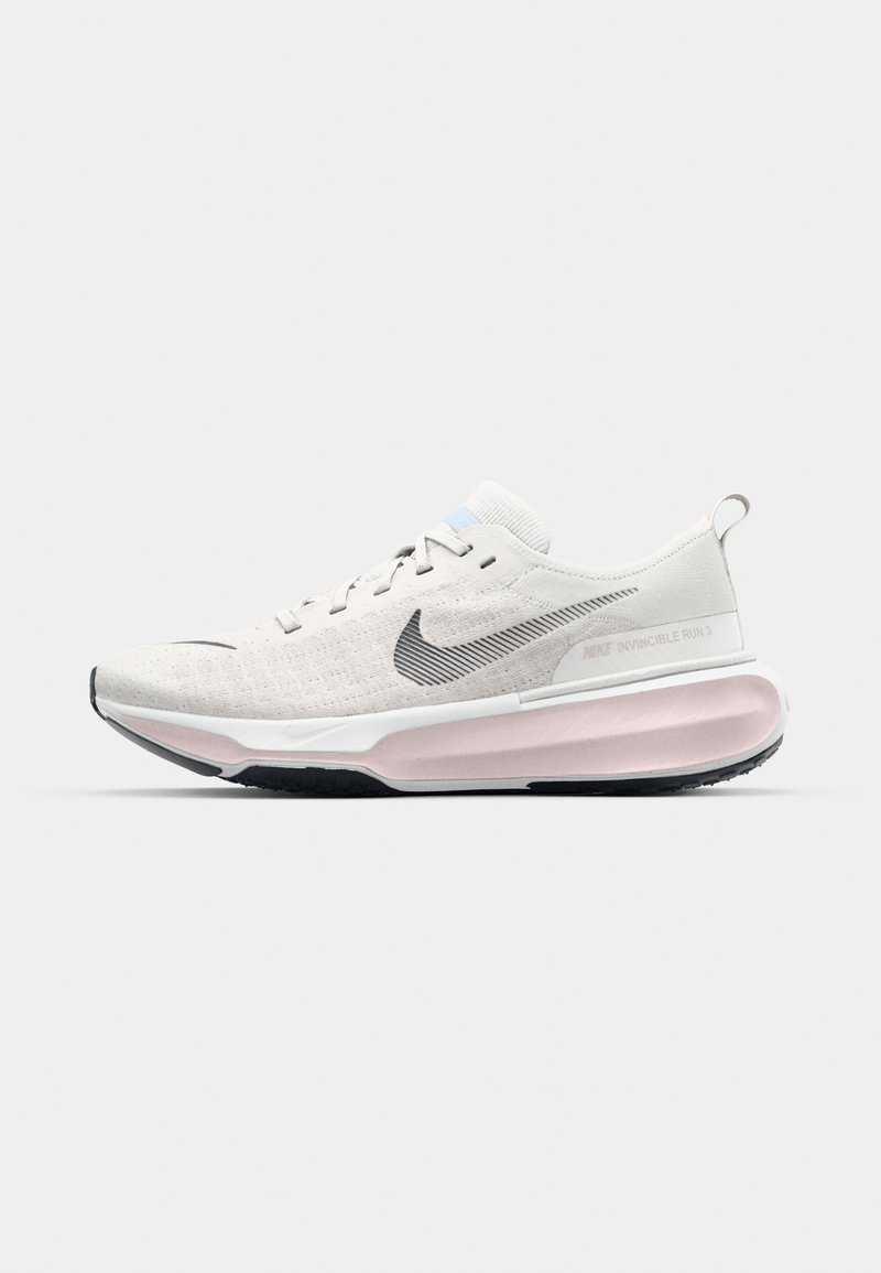 Chaussure de course Nike beige clair avec swoosh noir, semelle intermédiaire blanche, amorti rose et semelle extérieure noire, vue de côté sur fond blanc.